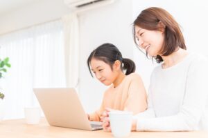 Photo of Asian parent or guardian and daughter happily looking at laptop computer.
