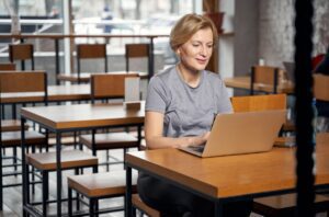 Photo of mature woman in athletic clothes working on a laptop in a cafe.