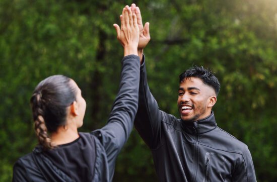 Active and fit physical education teachers high-fiving to celebrate, cheer, and congratulate each other outside.