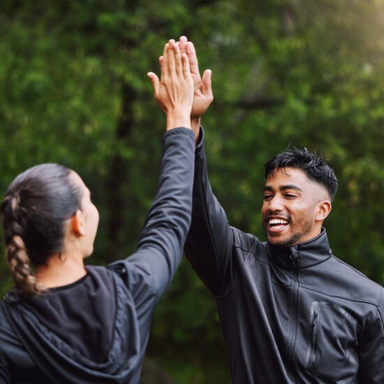Active and fit physical education teachers high-fiving to celebrate, cheer, and congratulate each other outside.