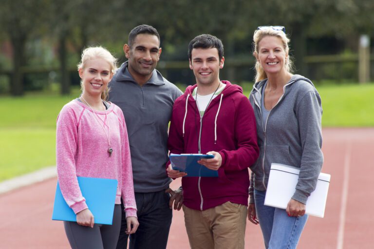 Two male and two female PE teachers standing on running track smiling at camera.